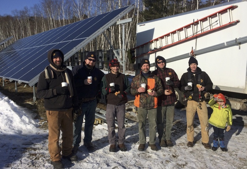 Below, the ReVision Energy Camden installation team warm up upon completion of Camden’s solar array in frigid temperatures. From left to right: Ren Floyd, Jerod Elder, Arthur Nerzig, Andy Lesko, Justin Milliken, and Hans (and Turner) Albee. (Photo courtesy Jennifer Albee)