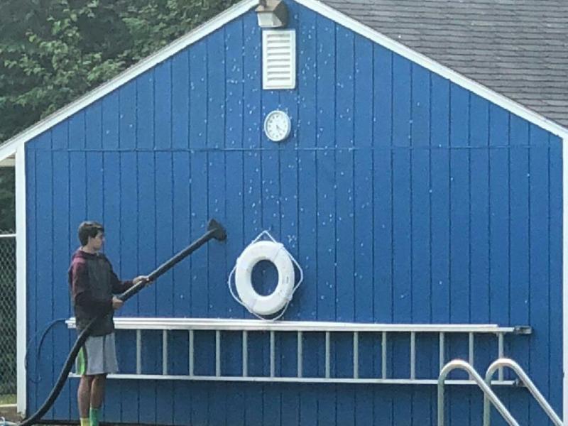 A lifeguard vacuums the moths off of a Belfast City Pool storage building. (photo courtesy Belfast Police Sergeant John Gibbs.)