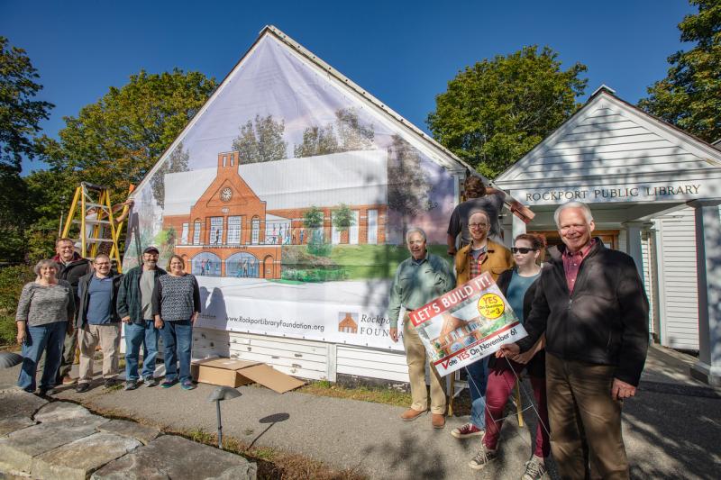 Members of the Rockport Library Foundation and community supporters unveiled a mural that depicts the new library at the site of the old and proposed future library, assuming voters approve Questions 2 and 3 this November.
L-R: Helen Shaw, Library Committee; Doug Cole, Select Board chairman; Ben Blackmon, librarian; Brian Filley and Ann Filley, Library Committee; Bill Leone, Capital Campaign Co-Chairman; Ben Odgren, Youth Services Librarian; Brandy Hare, Public Works Administrative Assistant; and John Viehman, Capital Campaign Committee. (Photo courtesy Rockport Library Foundation)