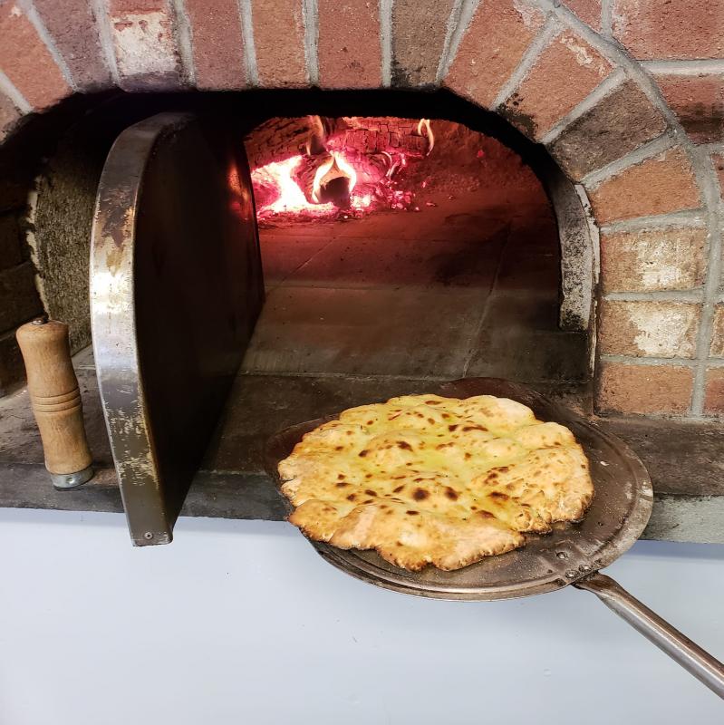 A cheese pizza coming out of the wood-fired oven. (Photo courtesy of The Stone Pizza Kitchen)