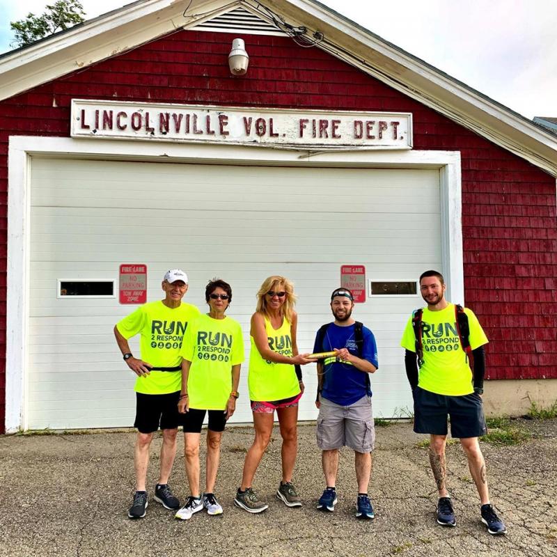 Sam Spinrad, in blue, hands off to Katie Daggett at the Lincolnville Fire Station, as Doug Johnstone, Carol Manley, and James Iandoli look on. (Photo courtesy Run2Respond)