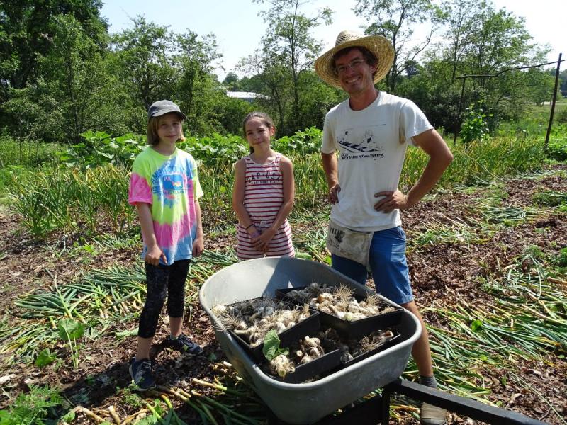 Gardening Coordinator David Wessel stands with two students and a wheelbarrow full of freshly harvested garlic. (photo by Erica Thoms)