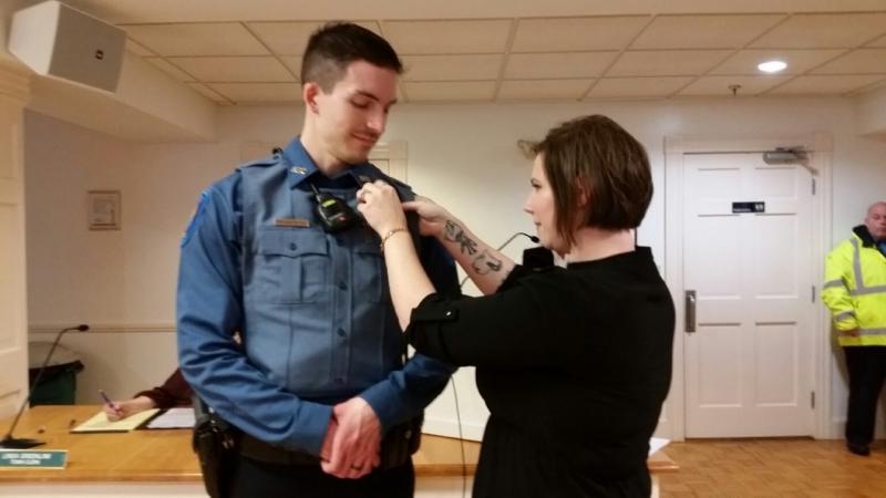 Jonathan Poole’s wife, Ashley, pins his badge on his police uniform during a pinning ceremony at the Rockport Select Board meeting Dec. 9. (Photo by Sarah Shepherd)