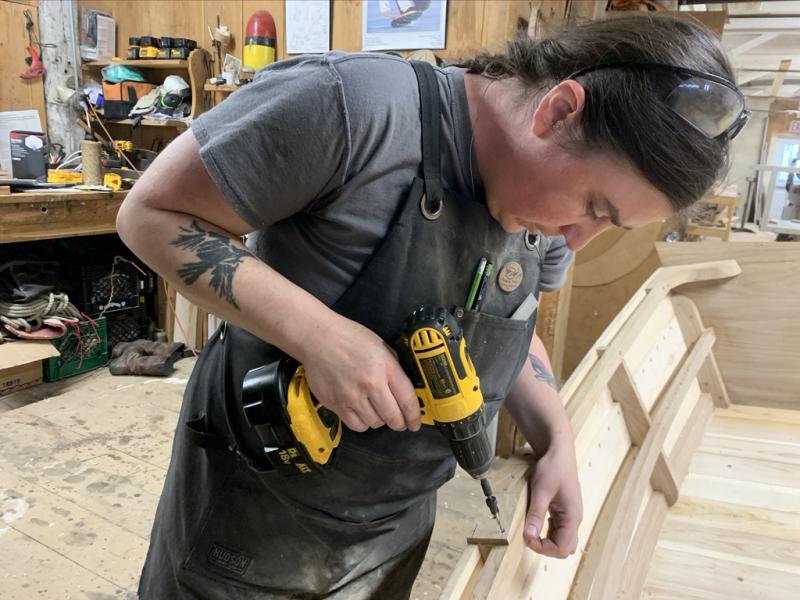 Emma and her almost completed skiff. Here, she’s drilling the fastener holes to be able to attach the oarlock pads to the hull. (Photo by Nate Hathaway)