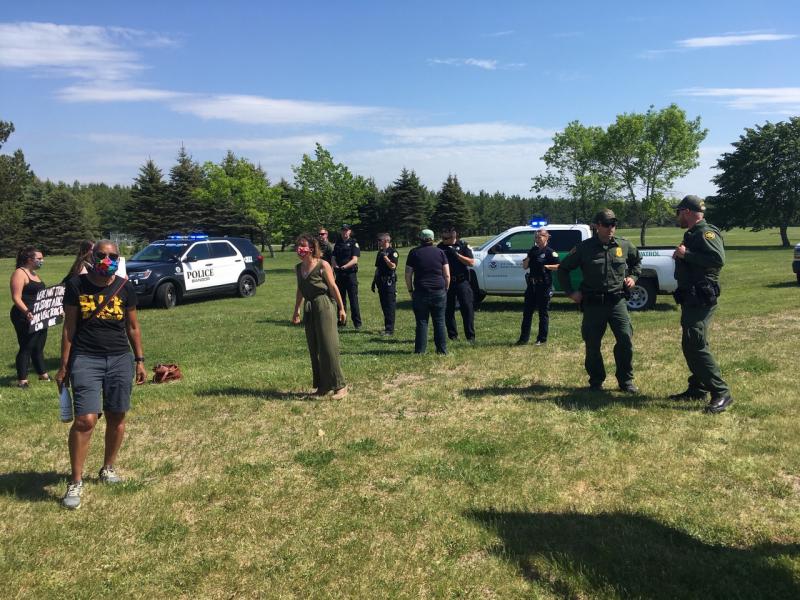 The police set up loosely organized defensive line to stop the protestors from heading to the airport fence. Protestors wore masks against the pandemic; the “safety” officers did not. The green uniforms belong to the border patrol. (Photo courtesy Molly Mulhern)