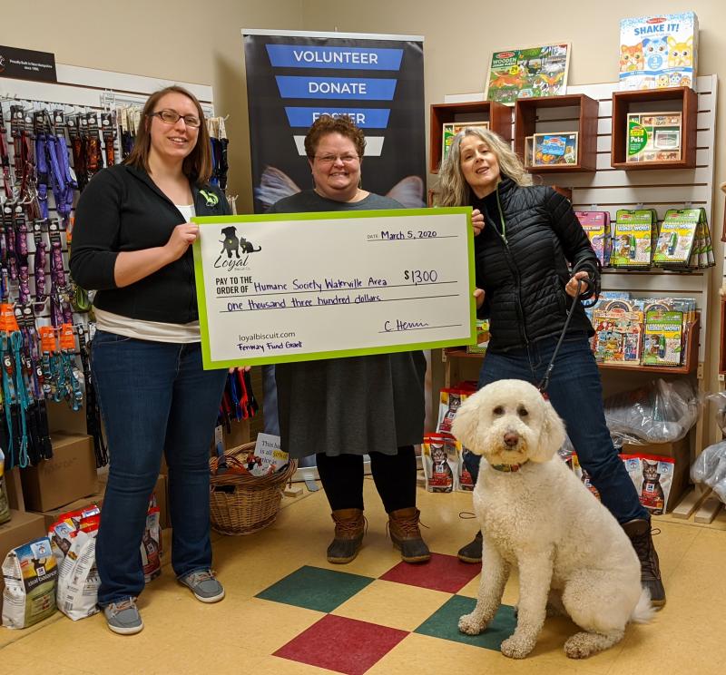 L to R: Chelsie Herrin (marketing manager for the Loyal Biscuit) presents a Fenway Fund grant check to Lisa Oakes (Humane Society Waterville Area executive director) and Dianna Demers (HSWA Board of Directors secretary) with her rescue dog, Sadie the Doodle. (Photo courtesy Loyal Biscuit)