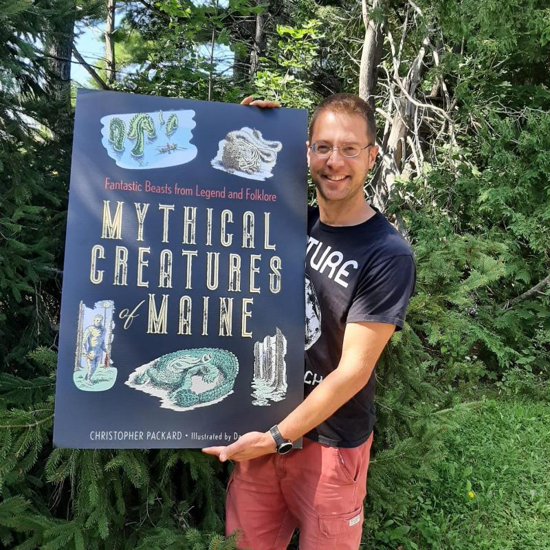 Packard with a giant poster of his book cover right before the book’s release. Photo courtesy Chris Packard.
