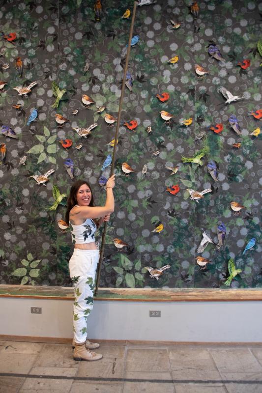 Artist Pippin Frisbie-Calder with her work Canceled Edition: the Art of Birding, in 2019. ‘Canceled Edition’ is a site specific installation of hundreds of handprinted birds, with the viewer invited to remove a bird from the wall to take home to simulate a local extinction. (Photo by Meg Turner)