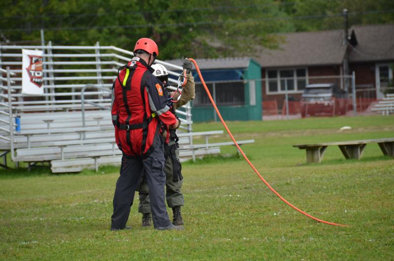 Assistant Fire Chief Andrew Lowe, buckled into a scream suit, waiting with District Forest Ranger Scott Maddox to be lifted by the orange line into the air. (Photo by Lynda Clancy)