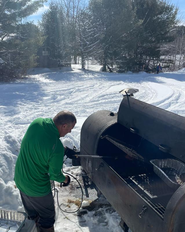 Grill Meister Andy Skrivanich, of Maine Outdoor Guides, lights the coals in his monster grill. (Photo by Ed O’Brien) Grill
