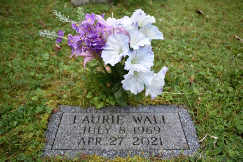 Laurie Wall, 51, had cerebral palsy. She died of “acute intoxication” of multiple prescription medications at a foster home in Cornville on April 27, 2021, medical examiner records show. Wall is buried at East Ridge Cemetery in Cornville. A bouquet of purple fabric flowers is placed by her grave. Photo by Samantha Hogan.