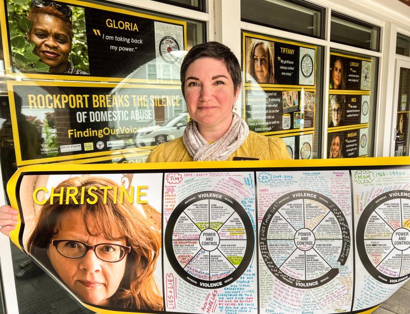 Julia Pierce, Deputy Director of the Rockport Public Library, stands in front of one of the 17 posters of survivors in the Finding Our Voices window exhibit that runs during October’s Domestic Abuse Awareness Month, and that can be viewed by standing outside. (Photo by Patrisha McLean)