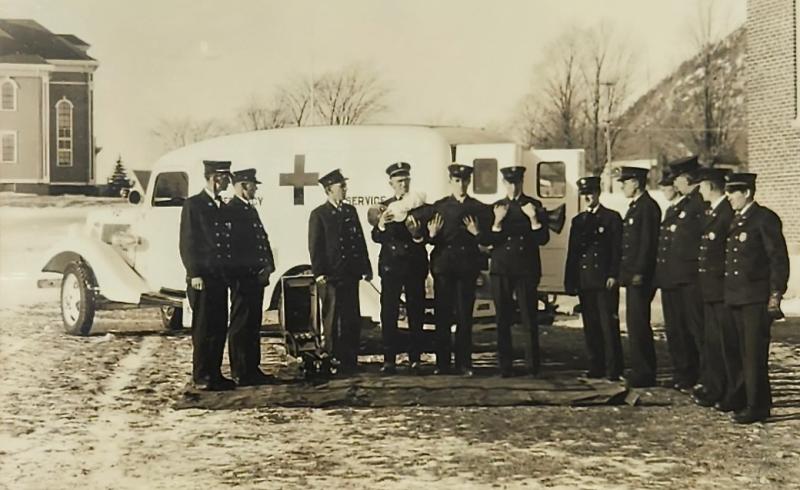 Camden Fire Department in 1936 with its new ambulance, a 1934 Ford. In their arms they hold then Fire Chief Allen Payson (he was alive, and no one can figure what they were doing, but likely they were laughing beneath their somber demeanor). From left to right, Joe Cote, Maurice Kennedy, Dick Damery, Clarence Mitchell, Clarence Thomas, Edwin Dodge, Hary Carl, A.B. Stevenson, Leon Poland, Percy Luce, Stan Dearborn, and Gene Thompson. The ambulance was housed on Washington Street across from the Town Office. (Photo courtesy Walsh History Center/Camden Public Library) Camden ambulance
