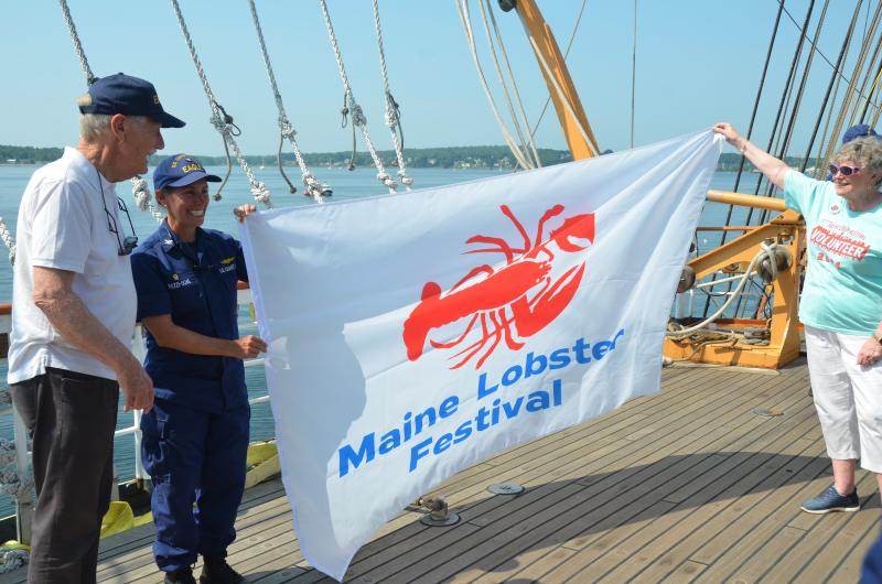 Senator Angus King, Capt. Jessica Rozzi-Ochs and a member of the Lobster Festival Committee unfurl a banner to help celebrate the annual Lobster Festival in Rockland.