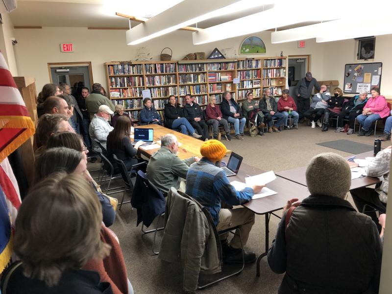 Near a 100 people tried to pack into the Bryant Room for the retail store hearing. (Sarah Masters photo) A group of people stand and sit in a meeting room.
