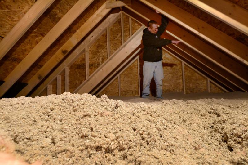 Michael McDonald, site supervisor at a new subdivision in Gorham, points out a detail in an attic filled 14 inches deep with blown cellulose insulation. Maine’s new energy code requires an unprecedented level of attic insulation, triggering a debate over balancing efficiency and housing affordability. Photo by Fred J. Field. a man standing in an attic.