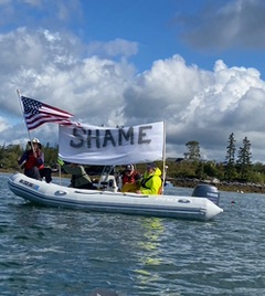 A boat circled the area with “shame” on a banner. (Photo by Nancy Galland)
A boat circled the area with “shame” on a banner. (Photo by Nancy Galland)