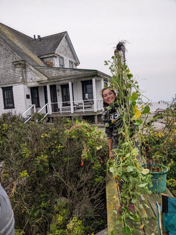 female holds up vine of vegetation in front of house