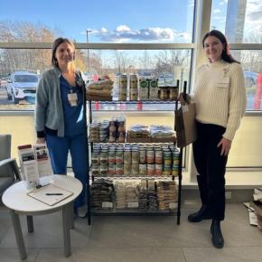 Two women pose with shelving unit of non-perishable food items