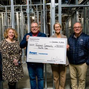 Six adults pose with oversized donation check