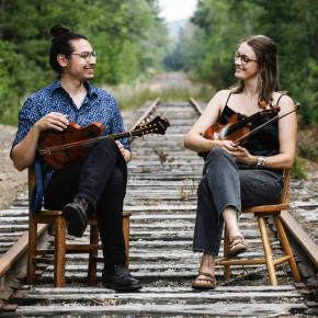 Two musicians seated on train tracks