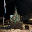 A short lit Christmas tree in front of a stone monument to War Veterans