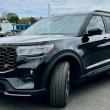 The red ST badge and black grille denote the 400-horsepower performance variant of the 2025 Ford Explorer; other visual clues include red brake calipers and these blacked-out 21-inch aluminum wheels. The view out over the high, squared-off nose is distinctly pickup-truck. This color is Agate black Metallic. 