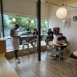 4 people in a coffee shop, 3 sitting and 1 wearing an apron, look off camera