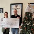 Woman and man hold oversized check next to Christmas tree
