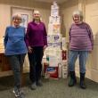 Three women pose in front of a tower of toilet paper