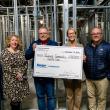 Six adults pose with oversized donation check