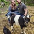 woman and man squat for photo with goat and chicken