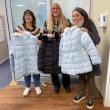 Three women pose with winter coats