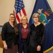 three women pose in front of state, federal flags