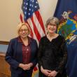 two women pose in front of state, federal flags