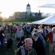 people gather on a lawn with the state house visible in the background