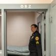 A corrections officer stands to the side in a doorway. 