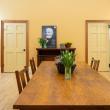 This image shows the Watts Hall boardroom as viewed from inside. In the foreground is a large wooden table with vases of fresh cut tulips. The back wall is a rich, golden color, and there are two doors in the wall, one leading to a closet, the other to the prep kitchen. There's a black and white photo of Captain Samuel Watts propped up on a credenza against the wall, and it's like he's looking out over the room. Photo credit: Nicole Langille Imagery.
