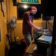 A picture of a man, DJ Souz, standing in front of DJ equipment. Hanging on the wall above his head is a road sign that says Myrtle St.