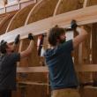 three men place board for a ship's hull