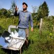 a man stands behind a solar oven in a field.