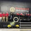 people in red shirts stand behind car on auction block 