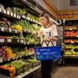 a woman places a vegetable into her shopping basket. 