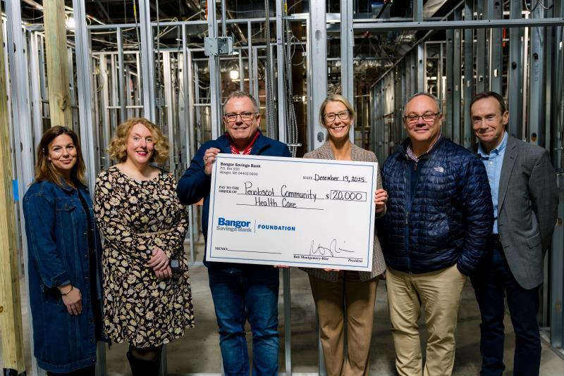 Six adults pose with oversized donation check