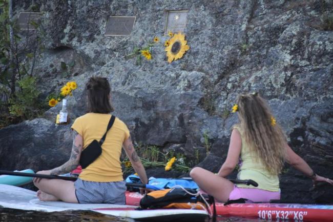 A sunflower helps identify a plaque for Sunshine Stewart that's mounted to a cliffside boulder on an island in Crawford Pond. (Photo by Sarah Thompson)
