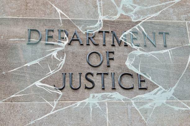 Department of Justice sign behind broken glass