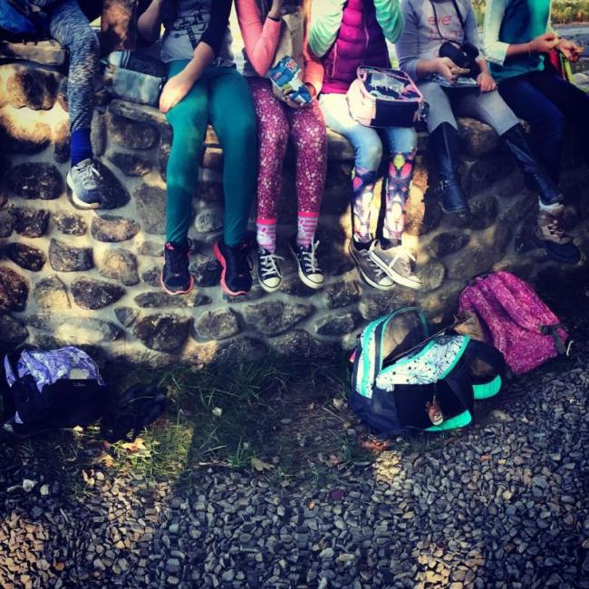 Kids sit on a brick wall while eating from lunch bags
