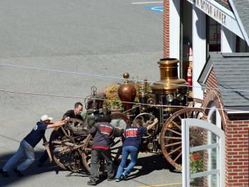 Andy Swift of Firefly Restoration in Hope, second from left, helps push Camden Fire Department's 1892 Amoskeag horse-drawn steam fire pumper into a bay at the station Tuesday, Sept. 11.