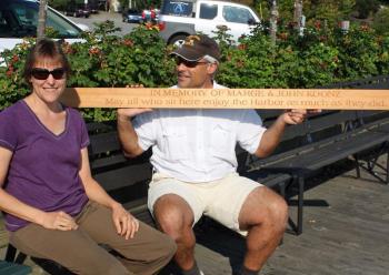 Camden Harbormaster Steve Pixley holds a newly engraved memorial bench plank alongside Marta Koonz.