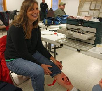 A volunteer "victim" shows off her newly applied moulage compound leg fracture and hypothermia-blue lip makeup. (Photo by Holly S. Edwards)